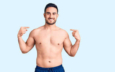Fototapeta premium Young handsome man wearing swimwear looking confident with smile on face, pointing oneself with fingers proud and happy.