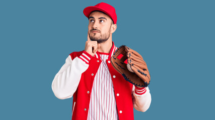 Young handsome man holding baseball gloves serious face thinking about question with hand on chin,...