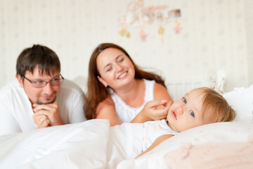 parents look at little girl sleep in bed in bedroom with crown.Princess birthday