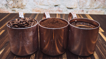 Three vintage old cups with coffee on wooden background. One with coffee beans, the second with...