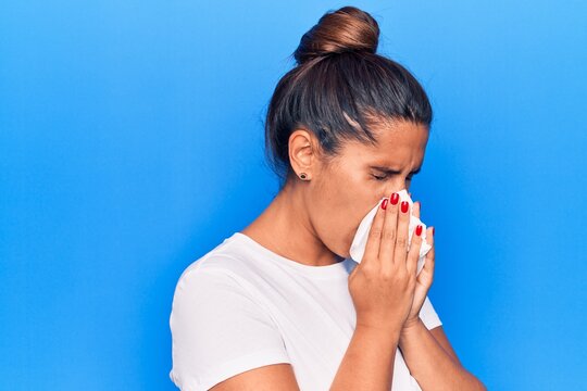 Young latin woman illness using paper handkerchief on nose. Standing over isoltated blue background