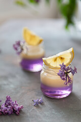 Lemon Vodka Shots Lemonade Cocktail with violet layer and lilac flowers on gray Background with fresh green leaves. Side view, close up. Bar menu, homemade shots drink recipe, summer party