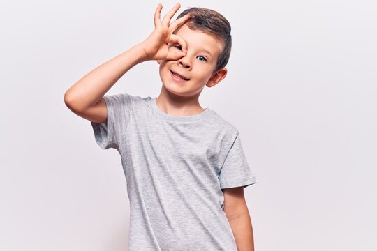 Cute blond kid wearing casual clothes smiling happy doing ok sign with hand on eye looking through fingers