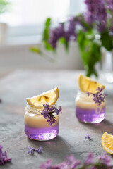 Lilac Vodka Shots drinks with vanilla liqour. Cocktail with Fresh lemon on gray concrete background with lilac flowers. Bar, restaurant menu, recipe. Side view, copy space