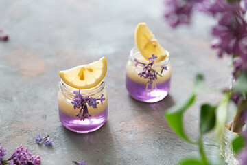 Lilac Vodka Shots drinks with vanilla liqour. Cocktail with Fresh lemon on gray concrete background with lilac flowers. Bar, restaurant menu, recipe. Side view, copy space