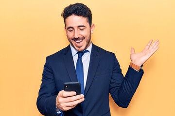 Young hispanic man wearing suit using smartphone celebrating victory with happy smile and winner expression with raised hands