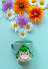 The original mug with decorative figurines made with their own hands. A lovely birthday present. Figures on the cup are fashioned hand made from colored clay. Fresh flowers background.