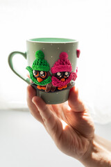 The original mug with decorative figurines made with their own hands. A lovely birthday present. Figures on the cup are fashioned hand made from colored clay. A hand holds cups. High quality photo