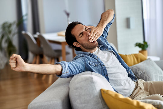 Tired man yawning while stretching on the sofa.