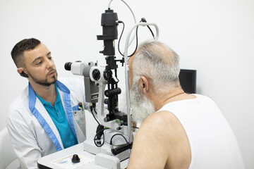 Doctor Optometrist examining bearded senior man eyes with special eye equipment.