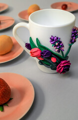 The original mug with decorative figurines made with their own hands. Figures on the cup are fashioned hand made from colored clay. Fruits and berries on a plates around. High quality photo