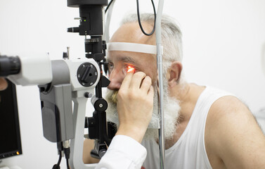 Doctor Optometrist examining bearded senior man eyes with special eye equipment.