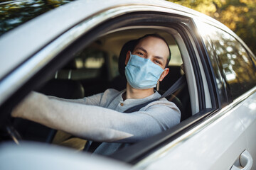 A man drives a car wearing medical mask during coronavirus outbreak. Taxi driver delivers his passanger to the destination. Social distance, new normal, virus spread prevention and treat concept.