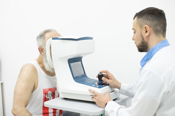 Doctor Optometrist examining bearded senior man eyes with special eye equipment.