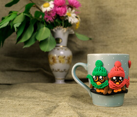 The original mug with decorative figurines made with their own hands. Figures on the cup are fashioned hand made from colored clay. Vase with fresh flowers on a background. High quality photo