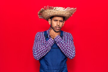 Young latin man wearing farmer hat and apron shouting and suffocate because painful strangle. health problem. asphyxiate and suicide concept.