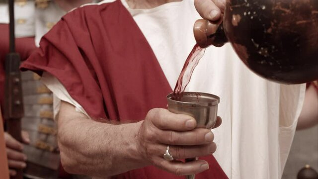 Man Pours Red Wine Into A Small Metal Glass And Passes It On