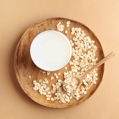 Oat milk in a glass on a wooden plate on a brown background. Milk substitute, milk for vegetarians. Copy space.