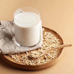 Oat milk in a glass on a wooden plate on a brown background. Milk substitute, milk for vegetarians. Copy space.