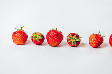 Ripe strawberries arranged in a straight line on a white background