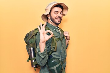 Young hispanic man wearing explorer hat and bakcpack doing ok sign with fingers, smiling friendly gesturing excellent symbol