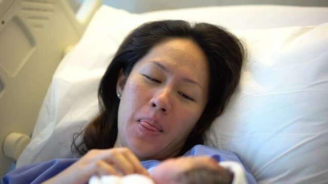 Asian Chinese Mother lying on hospital bed and carrying her newborn