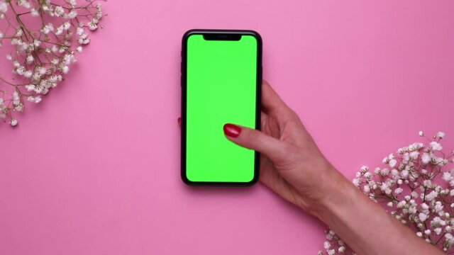 Mobile phone with green screen in hand on pink background top view, using technology, screen temperate , minimal concept