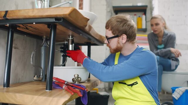 Professional plumber explaining woman how to fix sink pipes