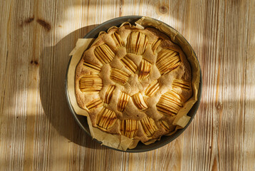 Round apple pie fresh from the oven on a wooden board with texture and warm tones.