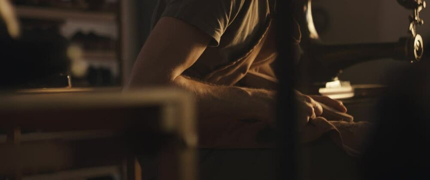 Shoemaker cutting leather insole on wooden shoe last with a knife in reopened small business workshop with magic light making traditional bespoke shoes