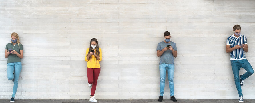 Young people wearing surgical mask using mobile phone keeping social distance - Millennial friends watching media trends on smartphones during corona virus outbreak - Youth and technology concept