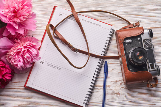 Beauty blog concept. Blogger or freelancer workspace with clipboard, notebook, retro camera, peonies and mobile phone on white bac.