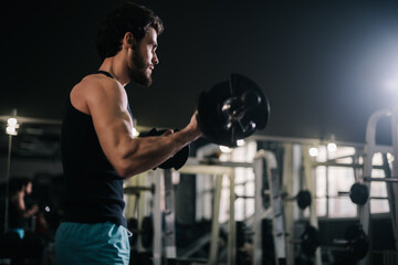 Handsome bearded young man with muscular wiry body wearing sportswear working out with barbell during sport workout training in modern dark gym. Concept of healthy lifestyle.