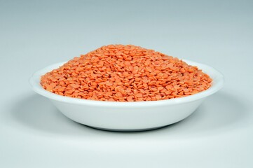 Red lentils in a white dish against a grey background.
