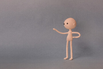 A toy man on a gray background with copy space. Cute amigurumi. Presentation PowerPoint or Keynote. Motivational phrase. Man with one hand points at object