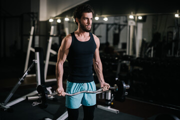 Strong bearded young man with muscular wiry body wearing sportswear working out with barbell during sport workout training in modern dark gym. Concept of healthy lifestyle.