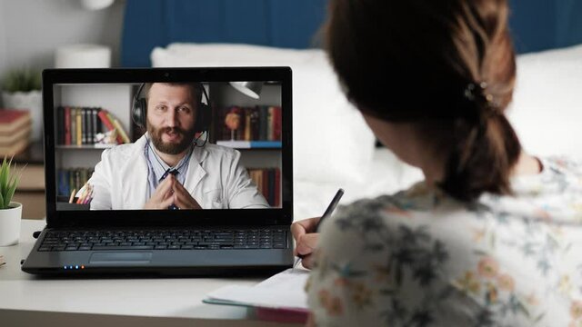 Doctor ophthalmologist online connection. Woman is talking with man in white coat on Internet video connection, doctor shows exercises for gymnastics for eyes, girl takes notes in notebook