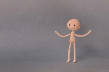 A toy man on a gray background with copy space. Cute amigurumi. Presentation PowerPoint or Keynote. Motivational phrase. The person is perplexed and spreads his hands to the sides.