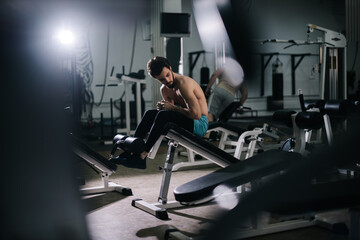 Fototapeta na wymiar Athletic bearded young man with muscular wiry naked torso doing abdominal crunches during sport workout training in modern dark gym. Concept of healthy lifestyle.