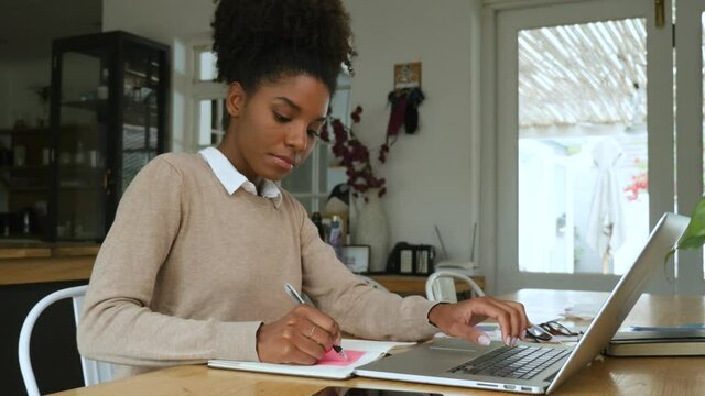 Young mixed race woman with afro working from home in front of laptop