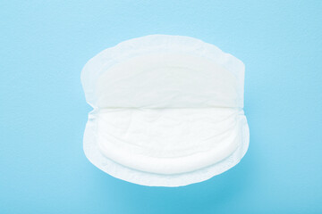 White breast pad on light blue table background. Pastel color. Bra and clothes protection in breastfeeding time. Closeup. Top down view.