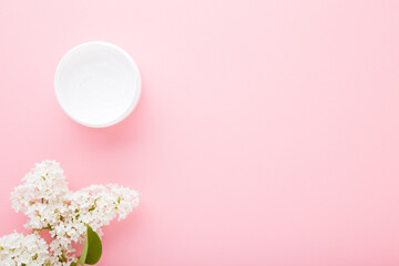 Opened jar of natural cream for women on light pink table background. Pastel color. Beautiful fresh white lilac blossoms. Care about clean and soft body skin. Empty place for text or logo. Top view.
