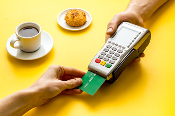 Payment by credit card. Hand hold card near terminal on yellow table