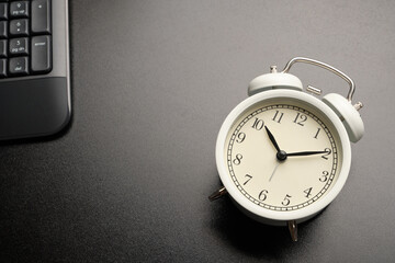 White vintage alarm clocks show 10:10 on black working desk with keyboard computer.