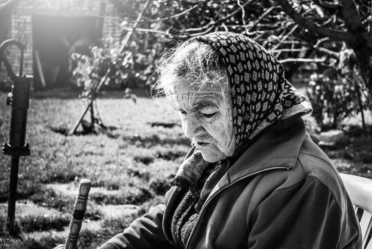 Old lady with a wrinkled face, sits on his farm yard, black and white photo