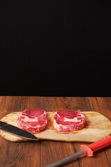 Two fresh raw rib eye steaks on a wooden cutting board, Premium range of beef. Butcher knife and steel, Black background.