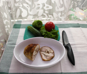 Freshly homemade chicken or turkey meat roll baked in the oven is on the ceramic pan next to vegetables and knife. Concept of cooking of healthy food at home. Step-by-step