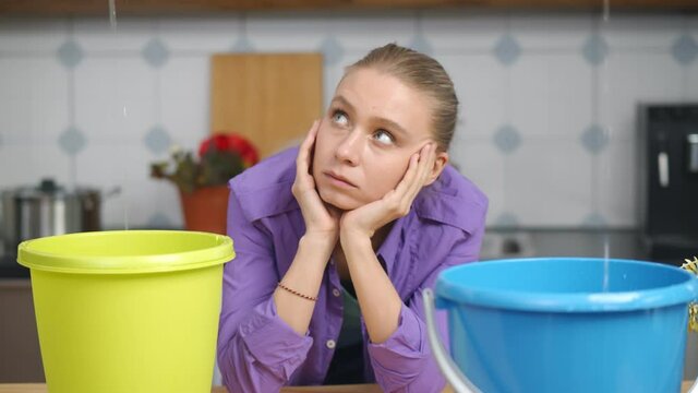 Woman looking at water leaking from ceiling into buckets in kitchen