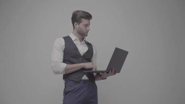 Young handsome businessman isolated on gray background using laptop 