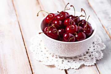 Sweet ripe red cherry in white bowl on vintage napkin. Summer natural low calories dessert. Wooden background. Close up macro. Copy space for text